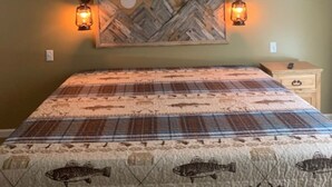 A bedroom with a bed, a ceiling fan, two wall-mounted lamps, and a decorative wall piece.