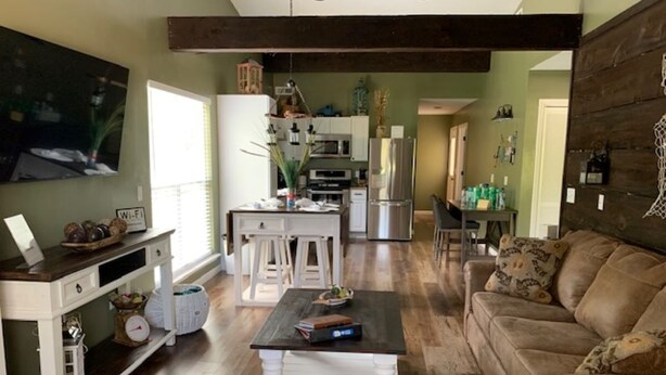 A spacious living area with a wooden floor, a brown leather sofa, a white coffee table, and a kitchen in the background.