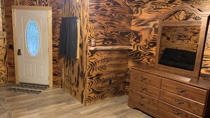 Una habitación con un diseño de pared de madera, una puerta blanca con un vitral, un aparador de madera con cajones y una alfombra estampada en el suelo.