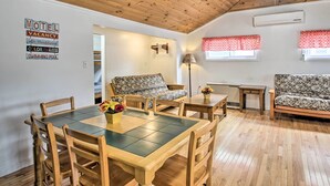 A room with a wooden ceiling, a dining table with chairs, two patterned sofas, a small table with a lamp, and a wall sign indicating amenities like a motel, air conditioning, color TV room, and swimming pool. - Homey Laconia Home w/ Private Porch & Grill (Laconia)