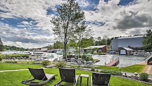 A riverside view with lounge chairs, a grill, and a dock with boats. - Charming Laconia Cottage: Walk to Weirs Beach (Laconia)