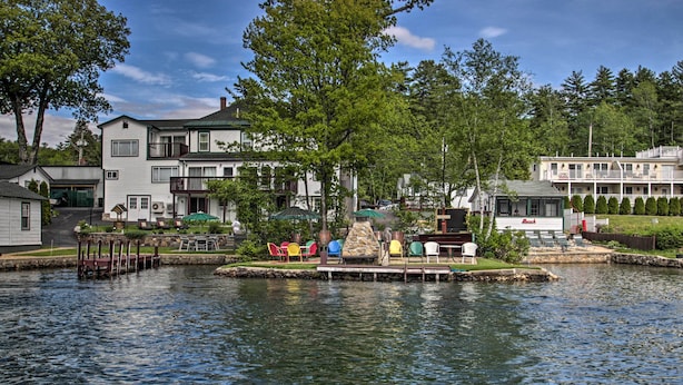 A lakeside property with a dock, colorful chairs, and a stone fire pit. - Charming Laconia Cottage: Walk to Weirs Beach (Laconia)
