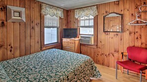 A wooden-paneled room with a bed, a television, and a red chair. - Charming Laconia Cottage: Walk to Weirs Beach (Laconia)