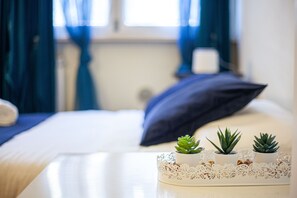 A neatly made bed with a blue pillow, a white bedside table with three small potted plants, and a lace doily. - [PISA STATION - CENTER] Elegant apartment with Netflix (Pisa)