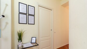 Ein Flur mit einer geschlossenen Tür, einem Empfangstresen mit Pflanze und Informationspostern an der Wand.