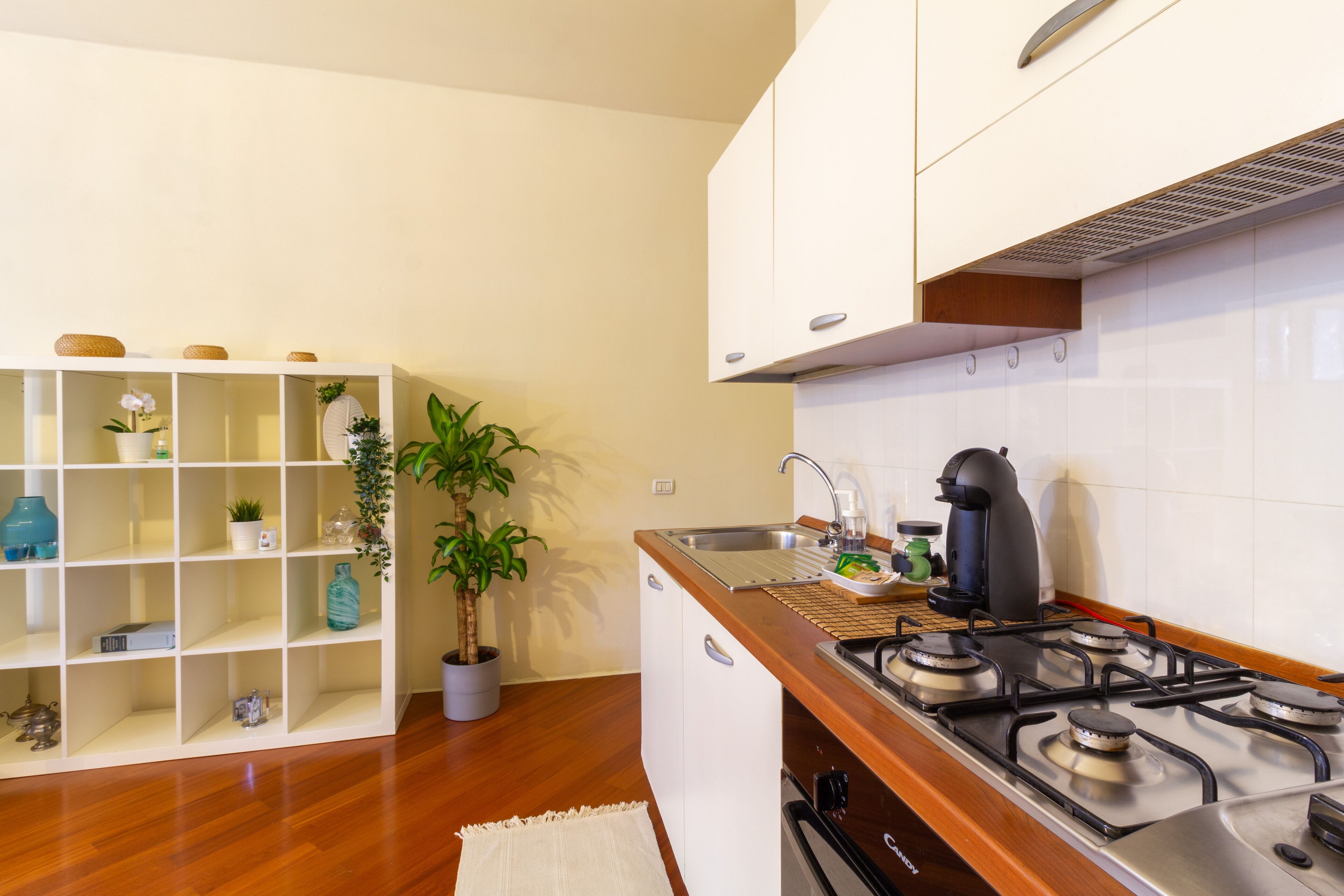 A modern kitchen with a gas stove, white cabinets, and a built-in shelf unit with decorative items.