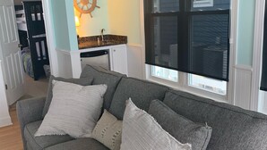 Una sala de estar con un sofá gris, un adorno de timón y una ventana con persianas.