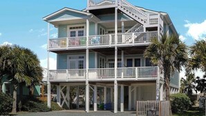 Una casa frente al mar de varios pisos, con un balcón en cada nivel, barandillas blancas y una vista despejada del océano.