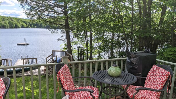 A deck with two chairs and a table, overlooking a lake with a dock and a boat. - Charming 2 Bedroom Lakefront Cottage in the Catskill Mountains (Roscoe)