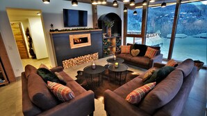 A cozy living room with a fireplace, large windows with a snowy view, and modern furniture.