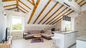 Un espacio habitable moderno con pared de piedra, vigas de madera, sofá, mesa de centro y zona de cocina.