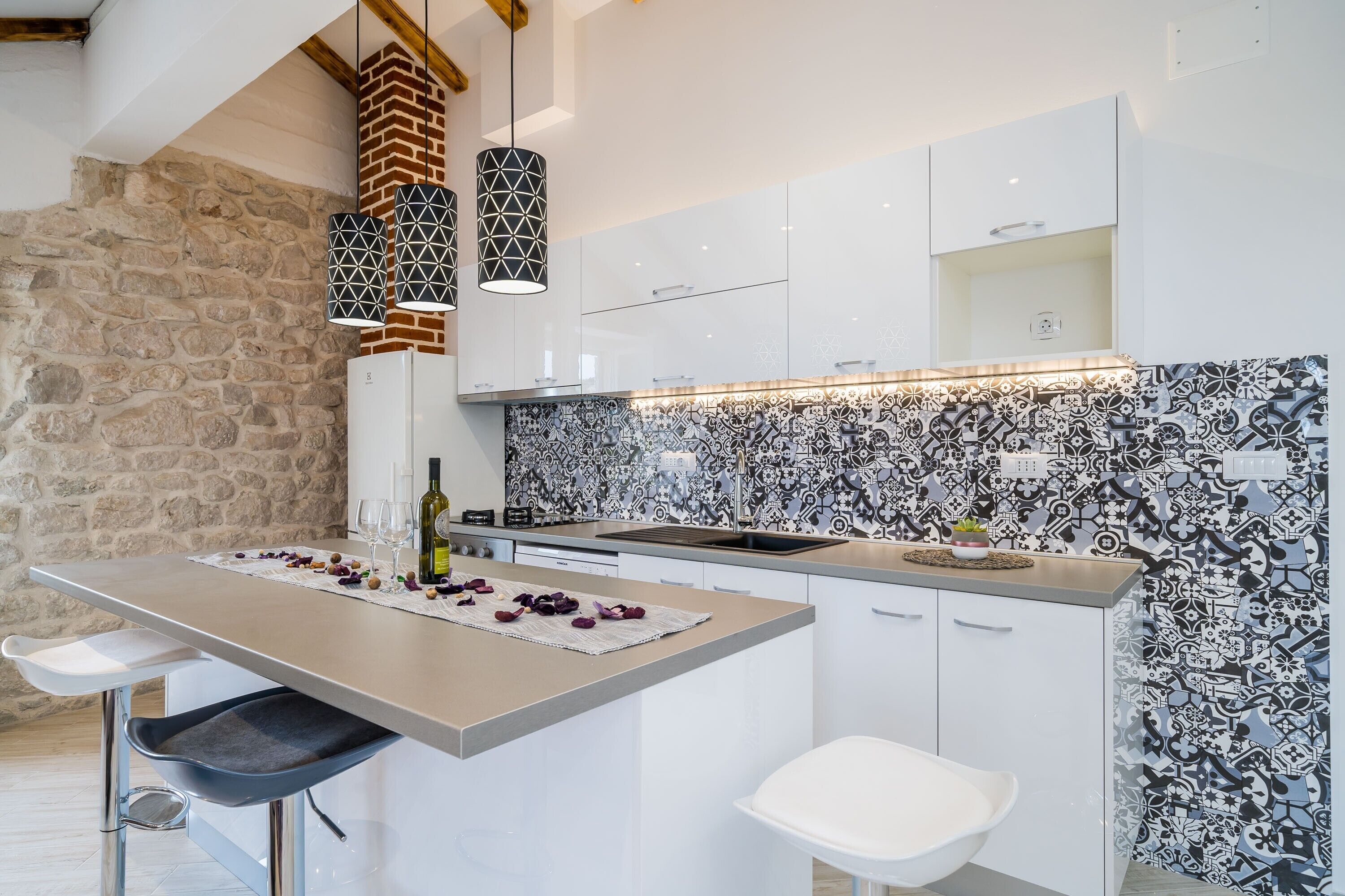 Uma cozinha moderna com ilha central, armários brancos e backsplash estampado.