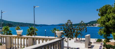 A seaside balcony with a view of the sea, palm trees, and a clear sky.