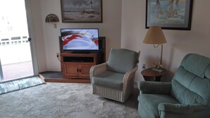 Un salon avec un téléviseur, deux fauteuils, une lampe et des œuvres d’art accrochées au mur.
