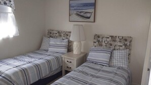Une chambre avec deux lits simples, une table de chevet avec une lampe et un tableau représentant une scène de plage.