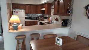 Une cuisine avec des meubles de rangement en bois, un plan de travail blanc, une machine à café et une table avec des chaises.