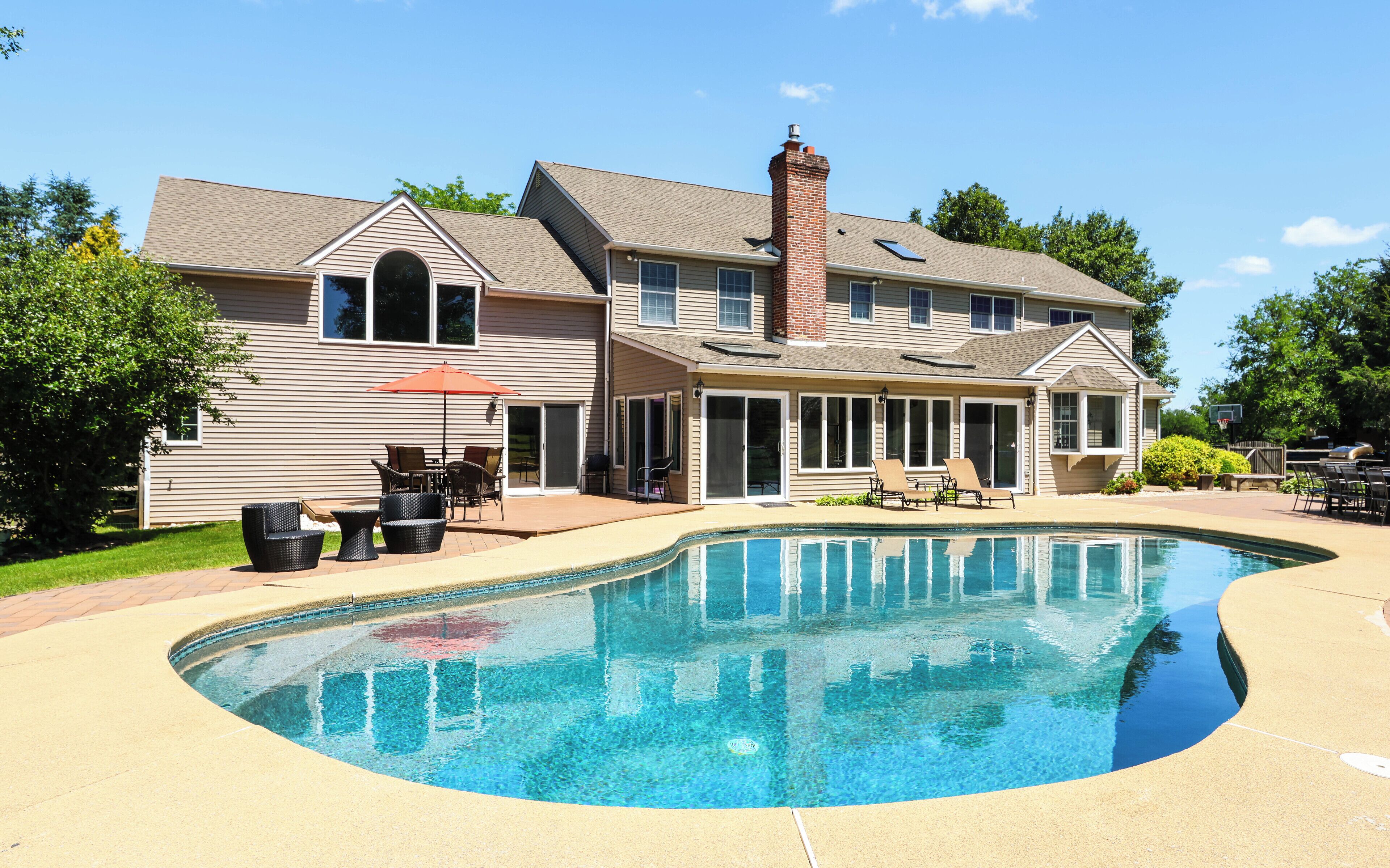 Une maison à deux étages dotée d’une piscine, de mobilier d’extérieur et d’un patio couvert.