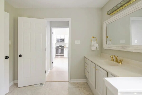 A modern bathroom with a white vanity, gold faucets, and a large mirror.