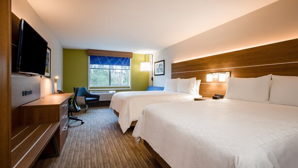 A hotel room with two beds, a desk with a TV, a chair, and a window with a view of trees. - Holiday Inn Express & Suites Deland South by IHG (DeLand)