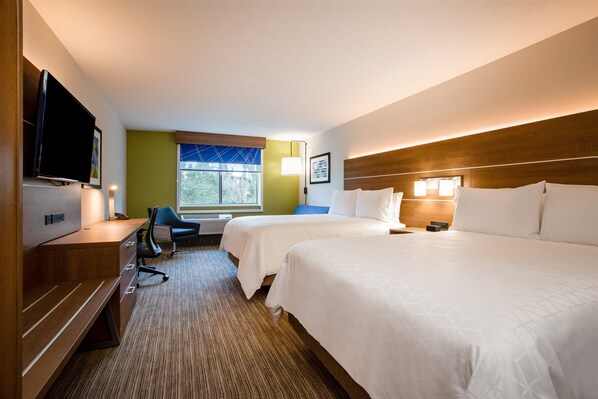 A hotel room with two beds, a desk with a TV, a chair, and a window with a view of trees. - Holiday Inn Express & Suites Deland South by IHG (DeLand)