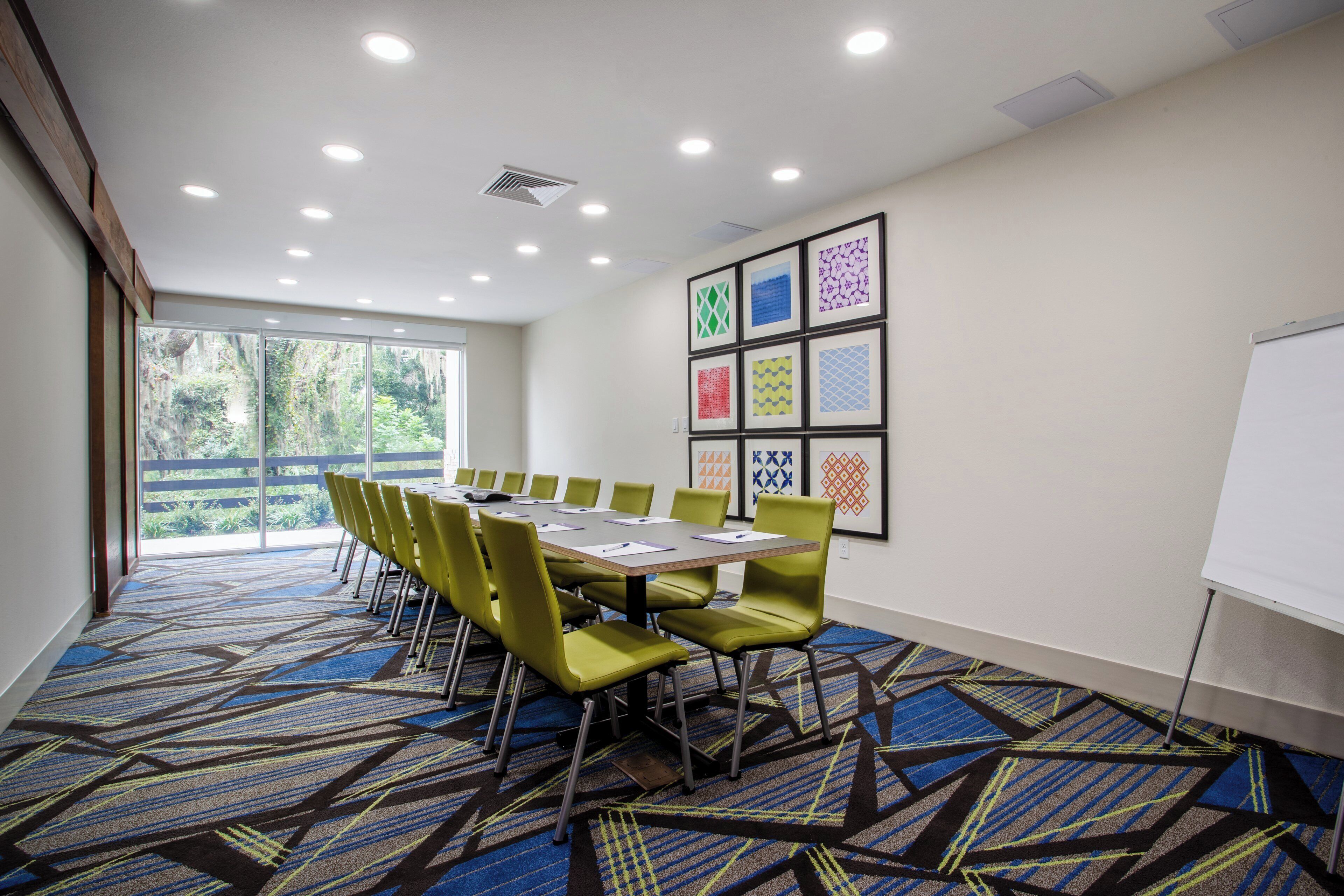 A conference room with a long table, green chairs, and a patterned carpet.