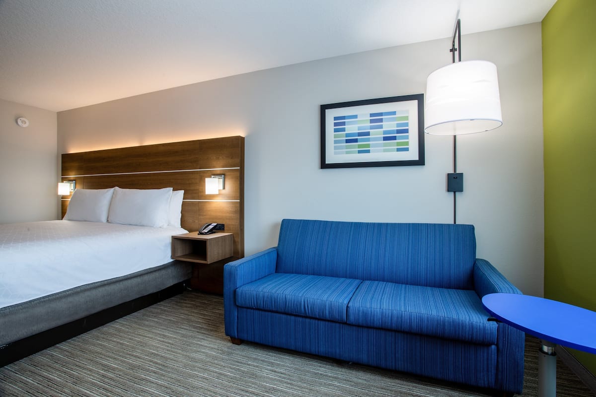 A hotel room with a bed, a blue sofa, a small table, and a wall-mounted lamp.