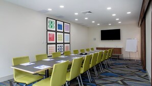 A conference room with a long table, green chairs, a whiteboard, and a projector screen. - Holiday Inn Express & Suites Deland South by IHG (DeLand)