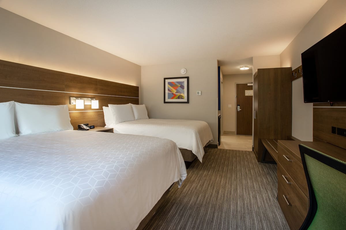 A hotel room with two beds, a desk, a television, and a framed picture on the wall.