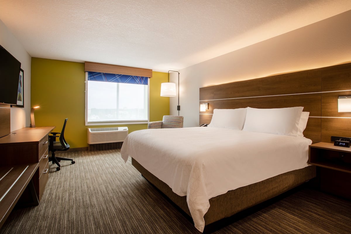 A hotel room with a large bed, a desk, a chair, a TV, and a window with a view.
