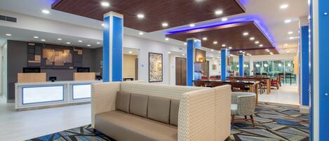 A modern hotel lobby with a reception desk, a sofa, and a dining area.
