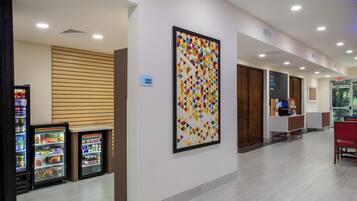 A hallway with vending machines, a wall-mounted artwork, and an exit sign.