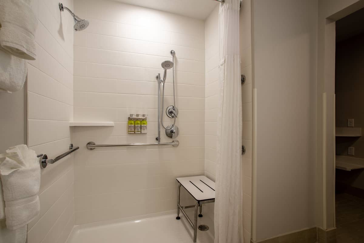 A bathroom with white tiles, a shower, a toilet, and a small table.