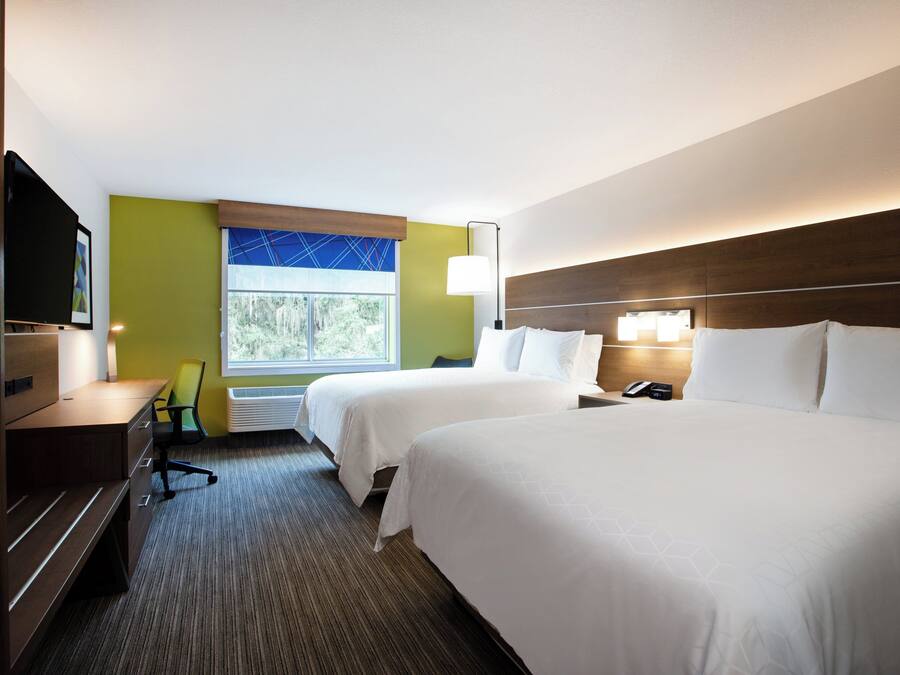 A hotel room with two beds, a desk, a chair, a TV, and a window with a view of trees.