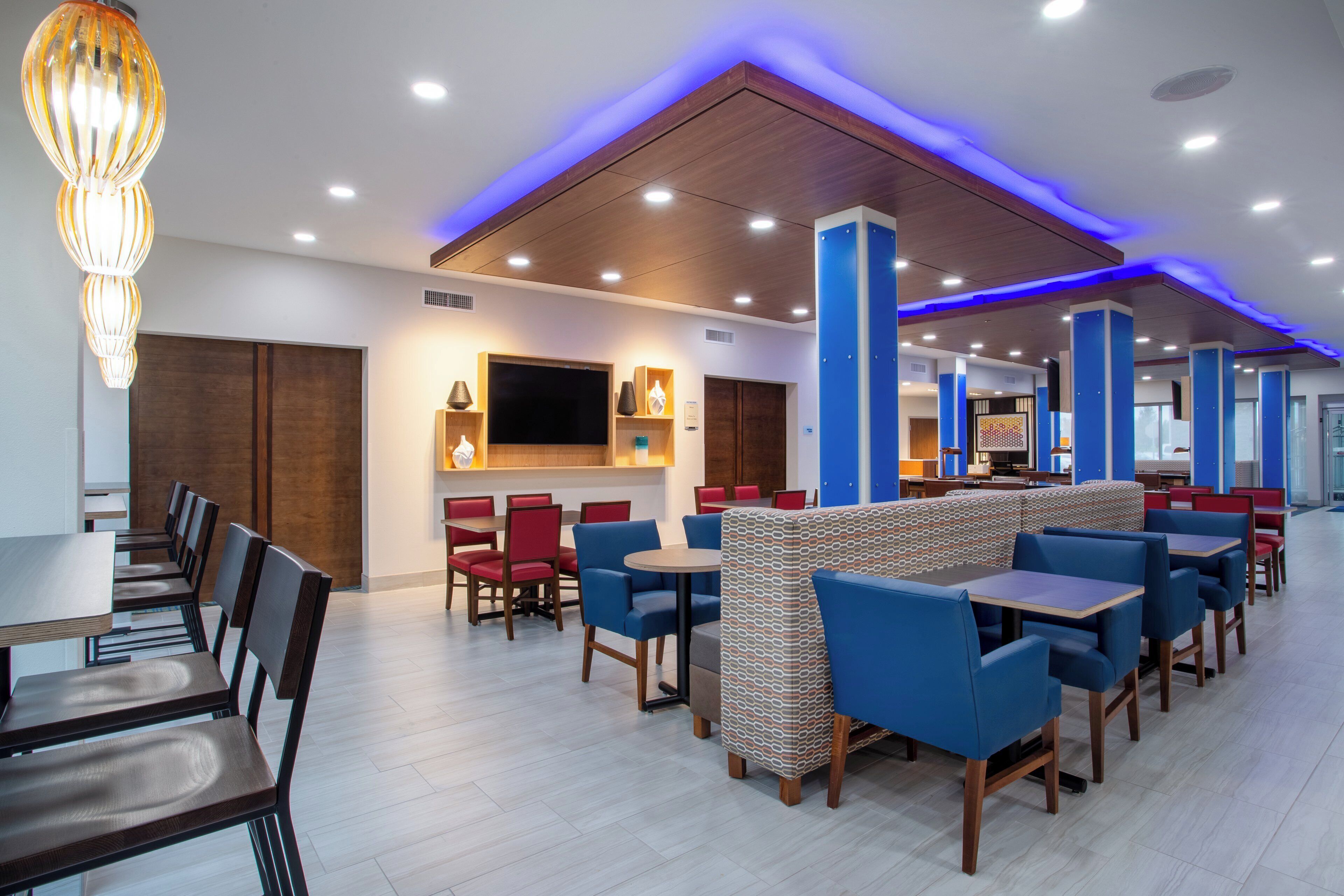 A modern restaurant with high ceilings, blue ambient lighting, and a variety of seating options including booths and tables.
