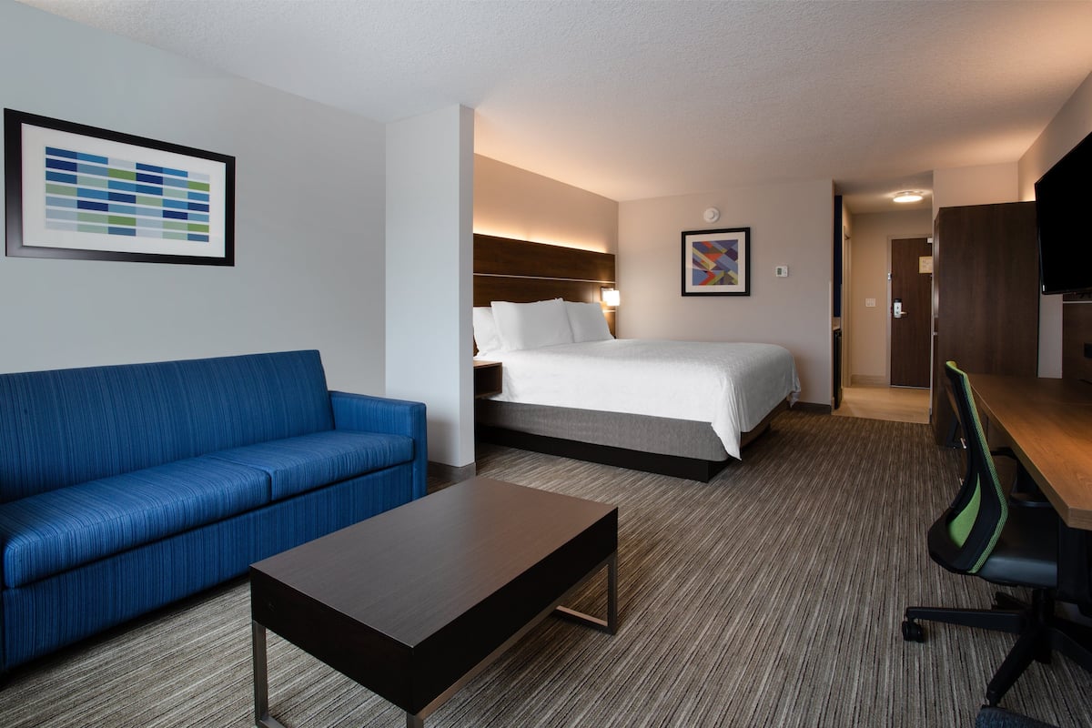 A hotel room with a blue sofa, a bed, a desk, and a chair.