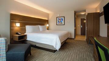 A hotel room with a bed, bedside tables, a desk, a chair, a TV, and a painting on the wall.