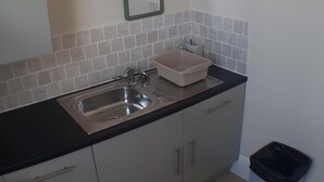 A kitchen with a stainless steel sink, a beige storage bin, and a trash bin. - Glen Villa Flat 1 - 4 Berth (Great Yarmouth)