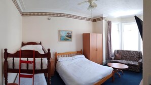 A hotel room with a wooden bed, a small sofa, a round table, and a painting on the wall. - Glen Villa Flat 1 - 4 Berth (Great Yarmouth)