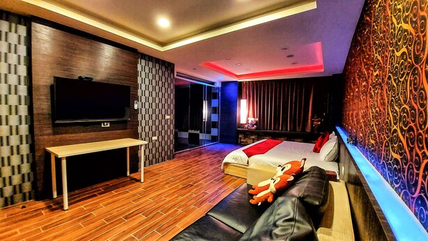 A modern hotel room with a large flat-screen TV, a wooden floor, a bed with a red blanket, and a patterned wall. - SUAO Backpackers (Suao)
