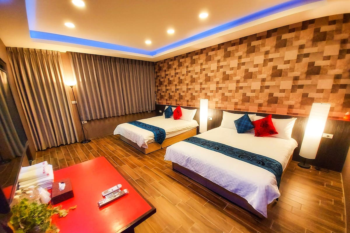 A hotel room with two beds, a red table with a remote control, and a wall with a pixelated pattern.