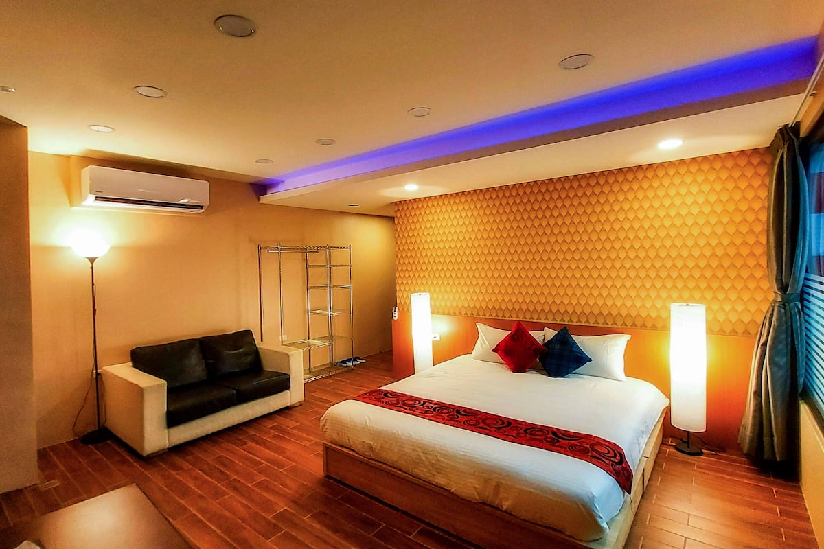 A hotel room with a bed, a sofa, a standing lamp, and a wardrobe.