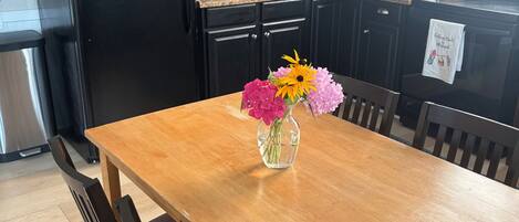 A kitchen with a black refrigerator, wooden cabinets, a granite countertop, a sink, and a vase with flowers on the table.