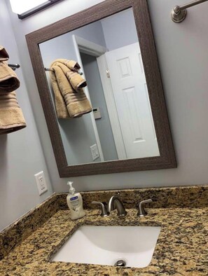 A bathroom with a granite countertop, a white sink, a mirror with a dark frame, and a towel rack with towels.
