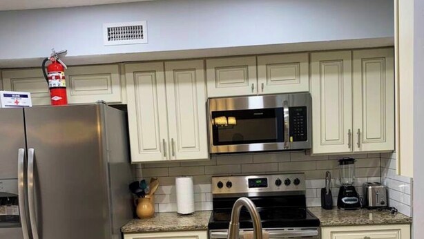 A modern kitchen with white cabinets, stainless steel appliances, granite countertops, and a built-in microwave. - Comfort Zone Palace Inn (Jacksonville)