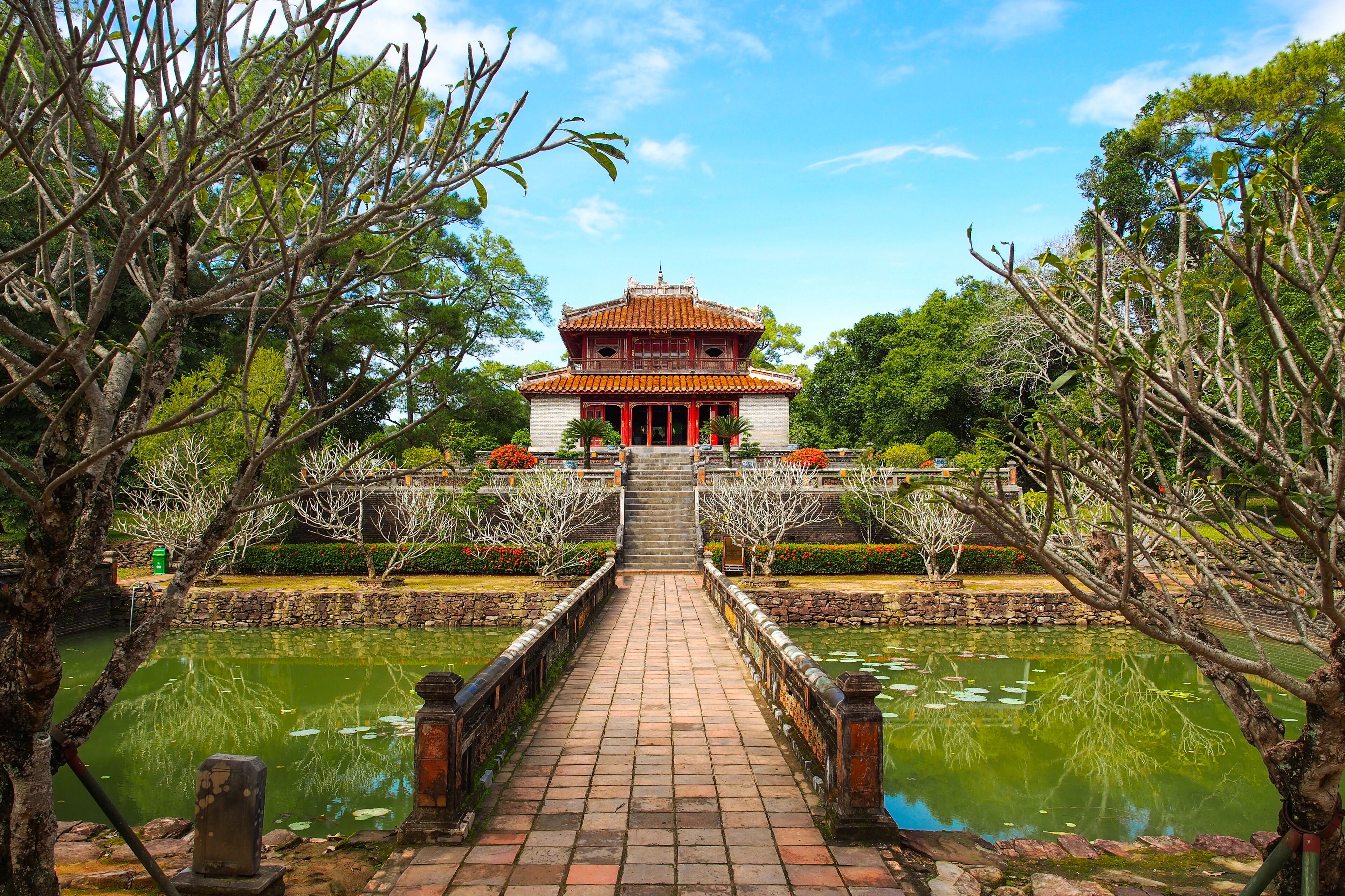 A traditional building with a tiled roof, a stone pathway leading to it, and a pond with reflections.