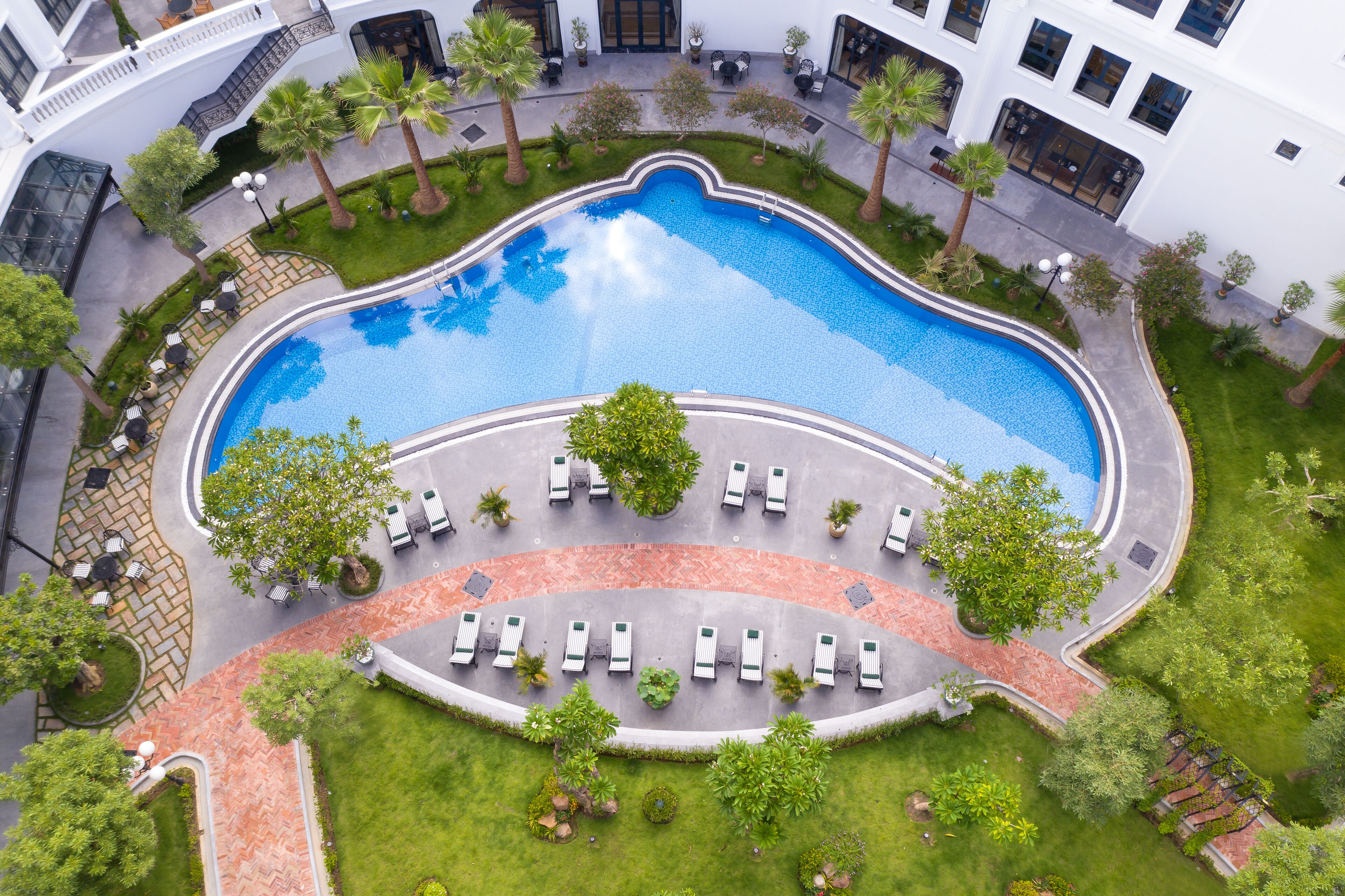 An aerial view of a hotel courtyard with a swimming pool, lounge chairs, and palm trees.