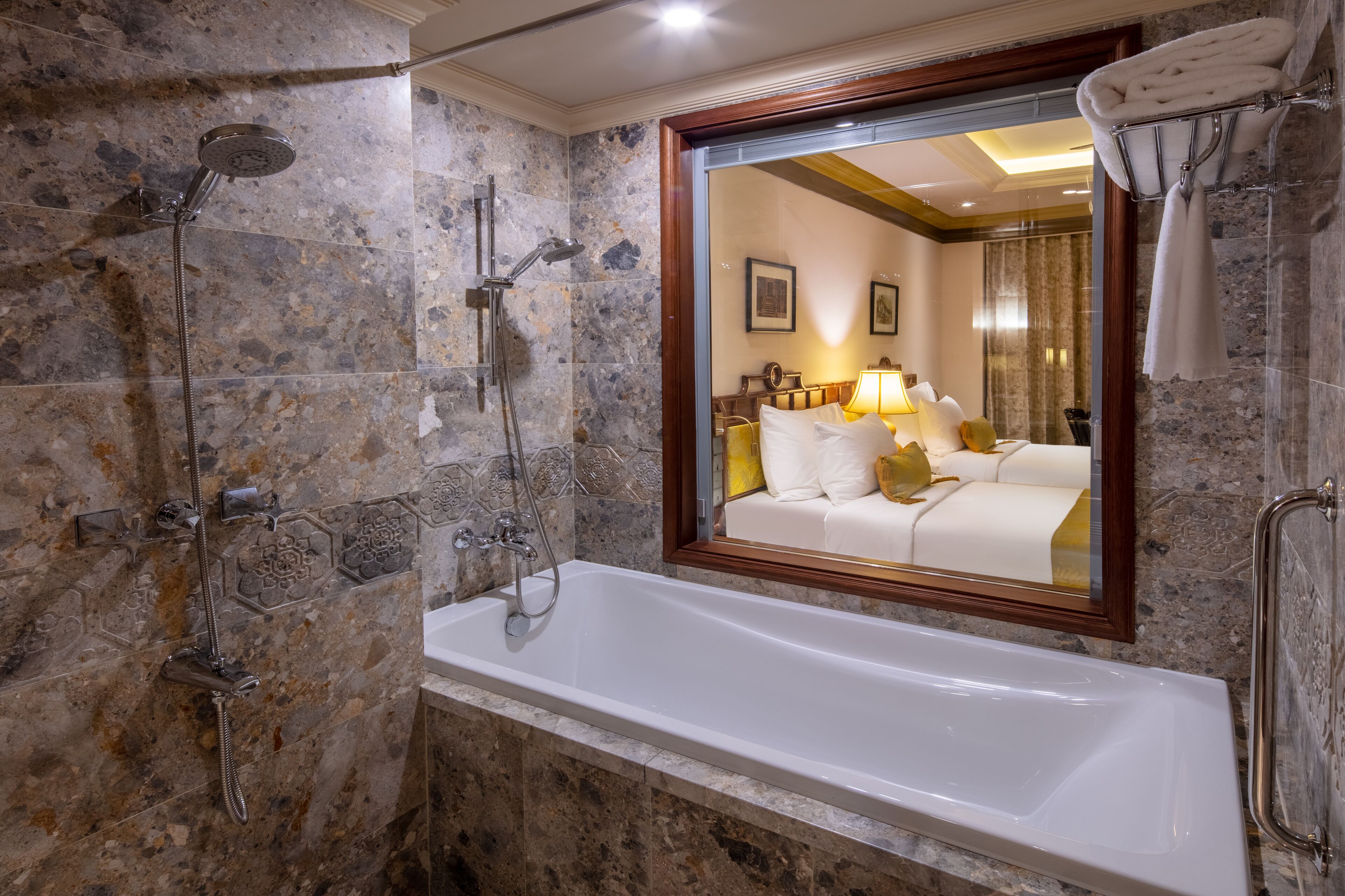 Un baño moderno con una bañera grande, ducha con múltiples cabezales y un espejo que refleja un dormitorio.