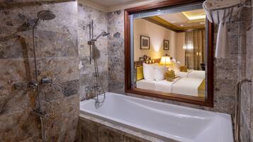 Un baño moderno con una bañera grande, ducha con múltiples cabezales y un espejo que refleja un dormitorio.