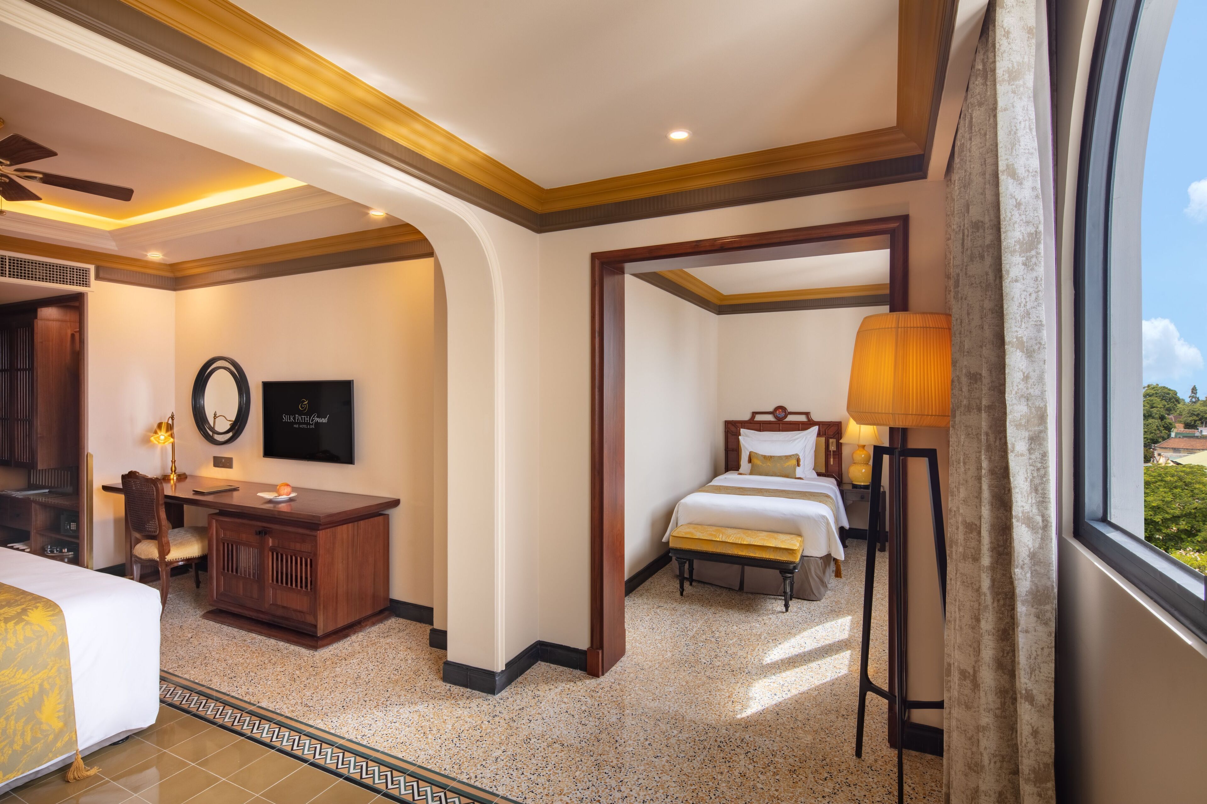 A hotel room with a bed, desk, and chair, a TV, and a view of the outdoors.