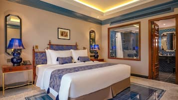 A hotel room with a large bed, two bedside tables with lamps, a ceiling fan, a large mirror, and a bathroom visible through a glass door.